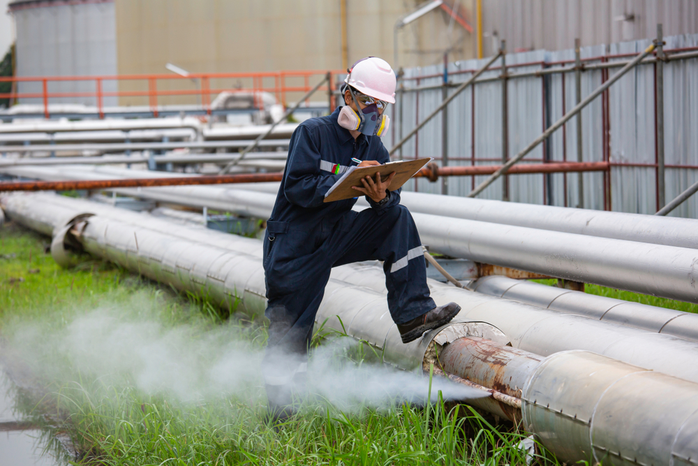 Man wearing gas mask inspecting leaking pipe